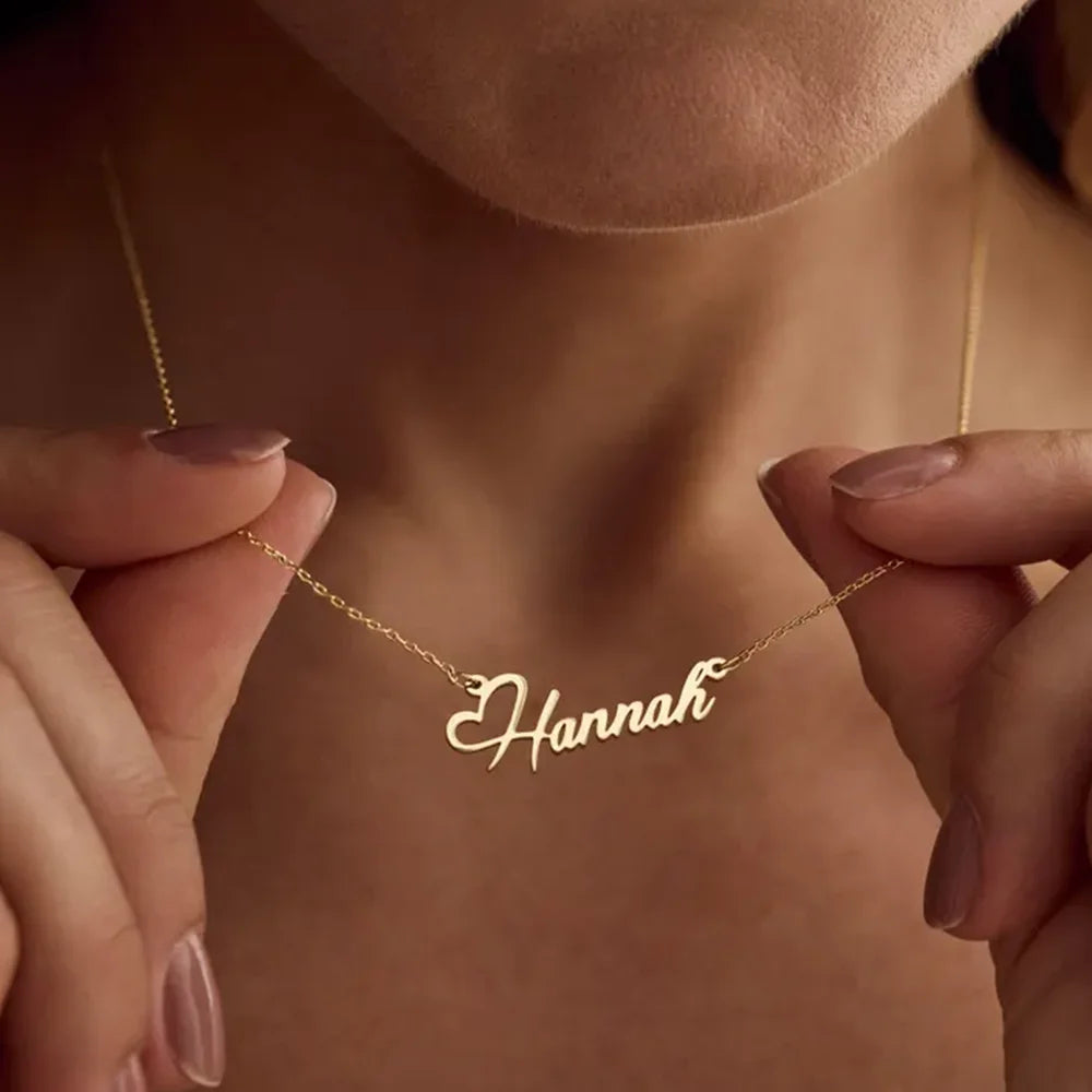 Gold necklace with 'Hannah' pendant held by hands against a blurred background