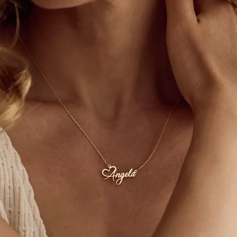 Gold necklace with 'Angela' pendant on a person wearing a beige top.
