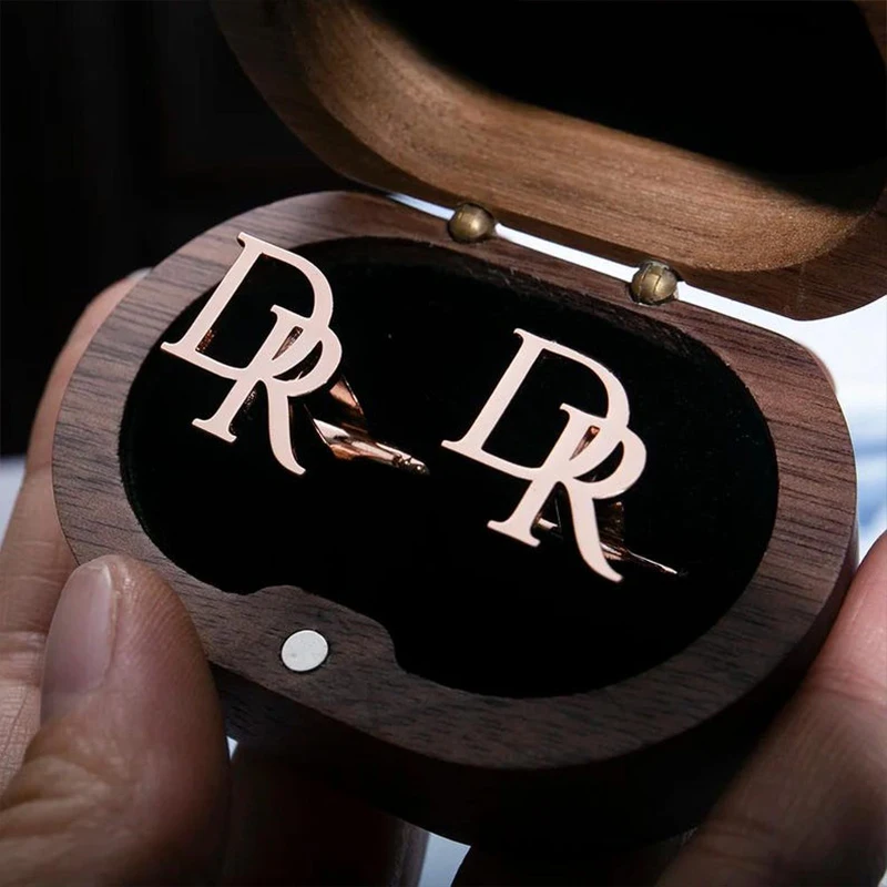 Wooden box with 'DR' initials and a pair of earrings inside, held by a hand.