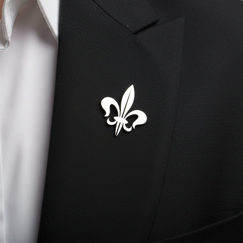 Silver fleur-de-lis lapel pin on a gray surface with a white background