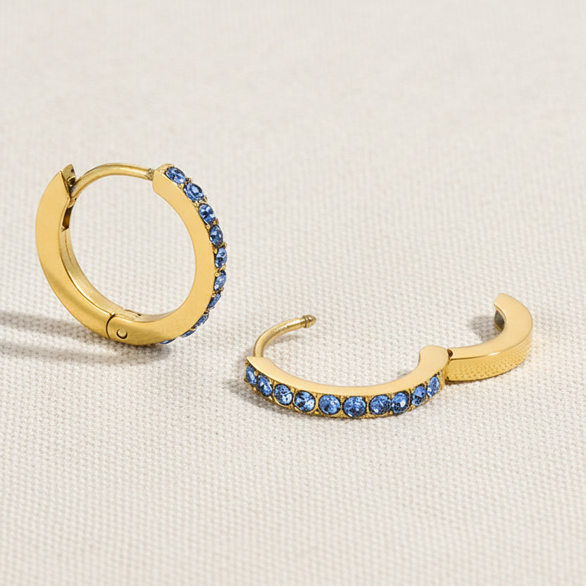 Gold hoop earrings with blue gemstones on a white background
