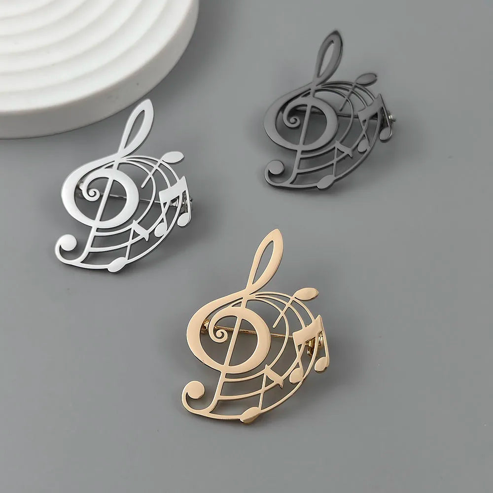 Three metallic brooches with music note designs on a gray surface.