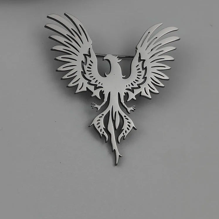 Silver phoenix brooch on a gray surface with a white ceramic plate in the background