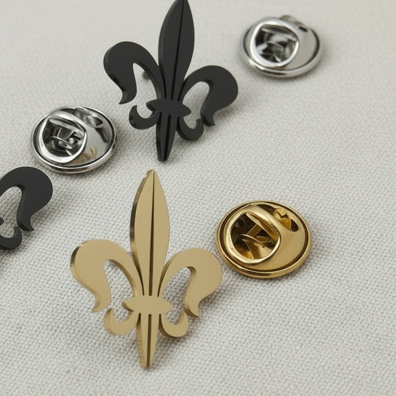 Fleur-de-lis pins in gold, silver, and black on a gray surface.