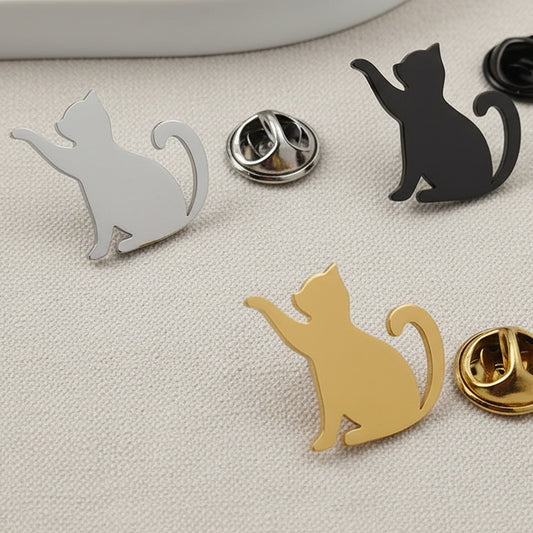 Cat-shaped pins in gold, silver, and black on a gray surface.