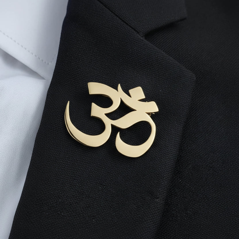 A set of brooches in the shape of the Om symbol in gold, silver, and black colors, displayed on a grey background.