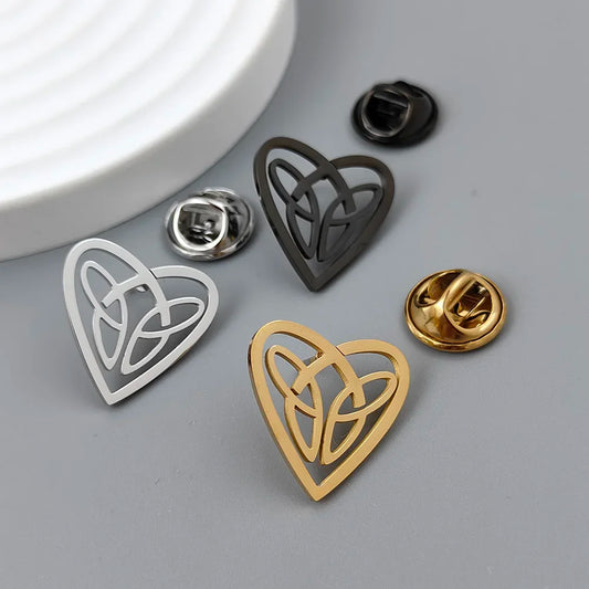 A collection of stainless steel brooches in the shape of a heart with Celtic knot patterns, displayed in silver and gold colors.