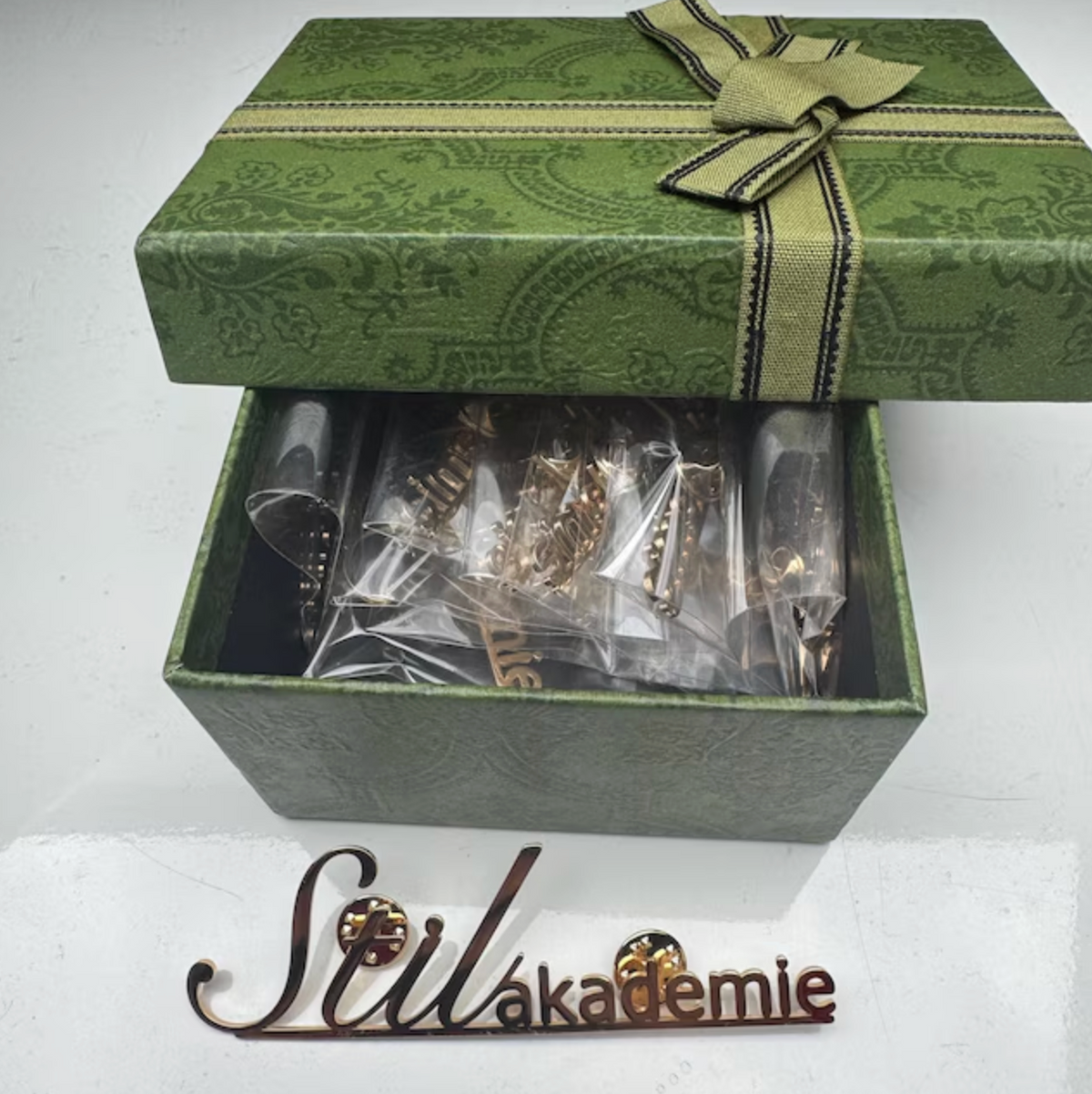 Green gift box with jewelry and 'Stilakademie' branding on a white background