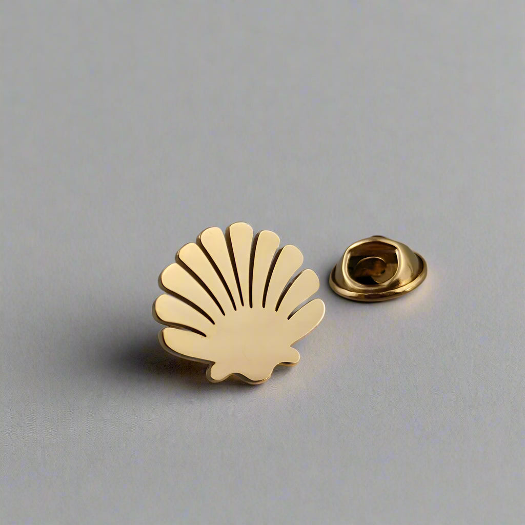 Gold shell-shaped pin on a gray surface with a white background