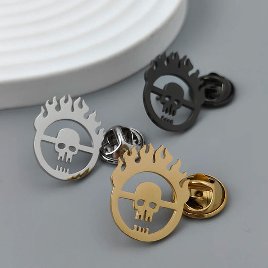 A set of metal brooches with a skull and flames design, displayed in black, silver, and gold colors.