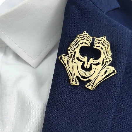 A set of four skull-shaped brooches in gold, silver, black, and gray colors, designed with a hollow pattern and attached to a fabric background.