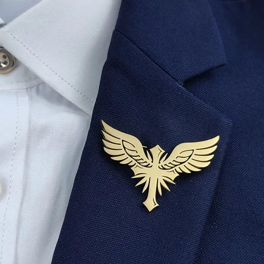 A selection of four gold and silver colored brooches with winged designs, displayed on a grey background and pins shown in different angles.